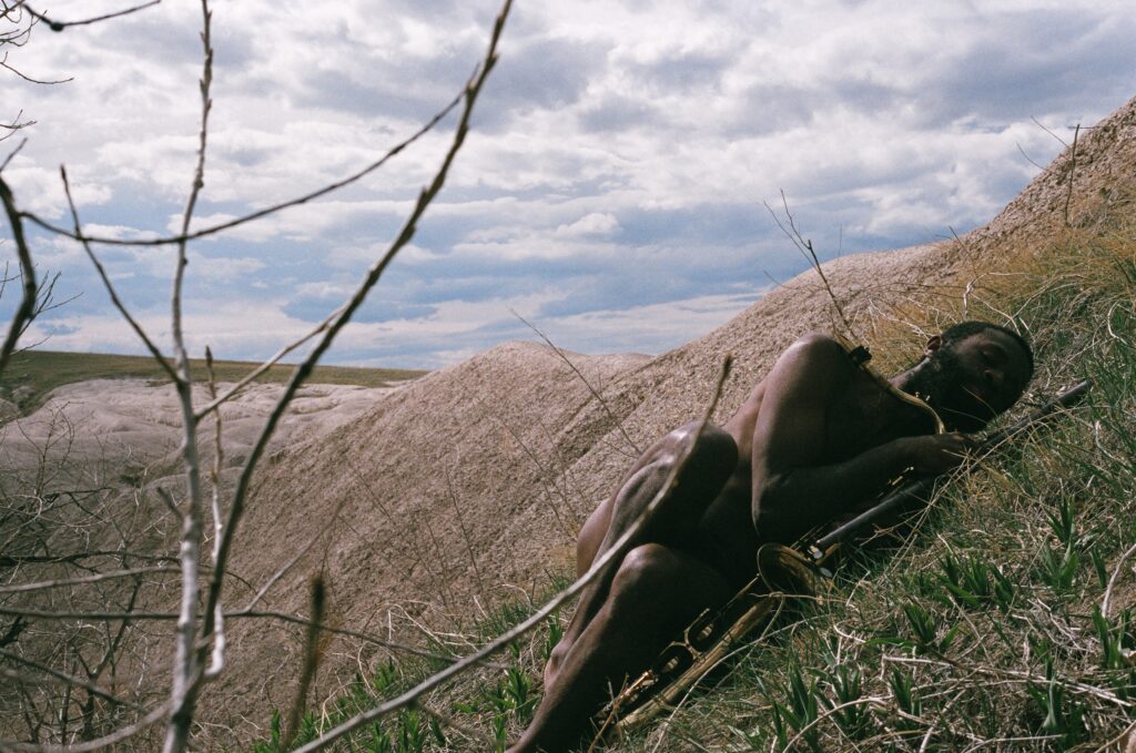 A mostly nude dark-skinned person laying on a barren hill.