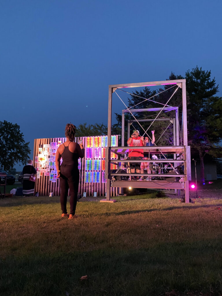 A wood and metal structure pictured at twilight with a single onlooker.